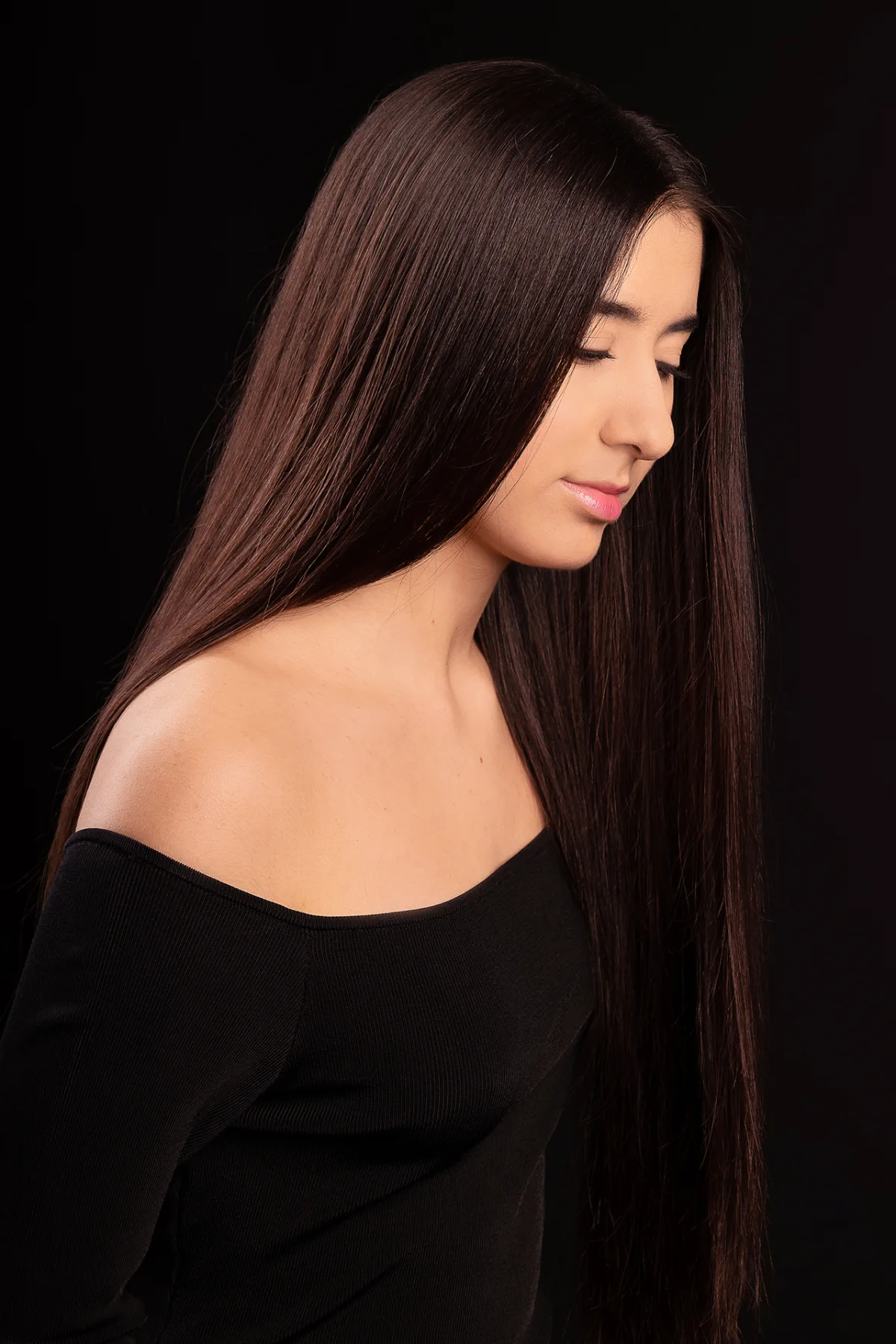 Beauty portrait of a young woman in profile, long straight brown hair, black studio backdrop