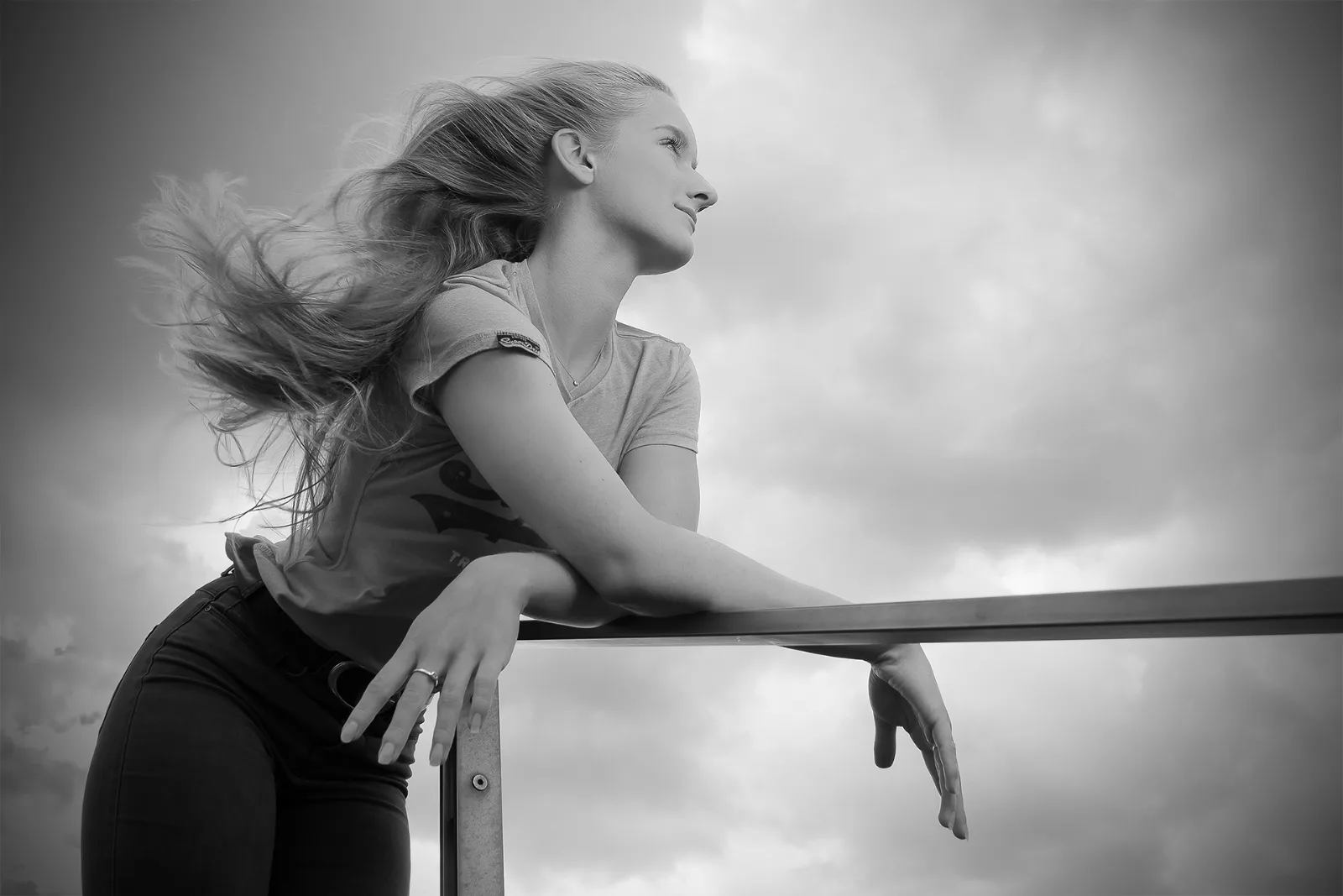 Black-and-white beauty portrait of a young woman with her hair caught by the wind, an overcast sky behind