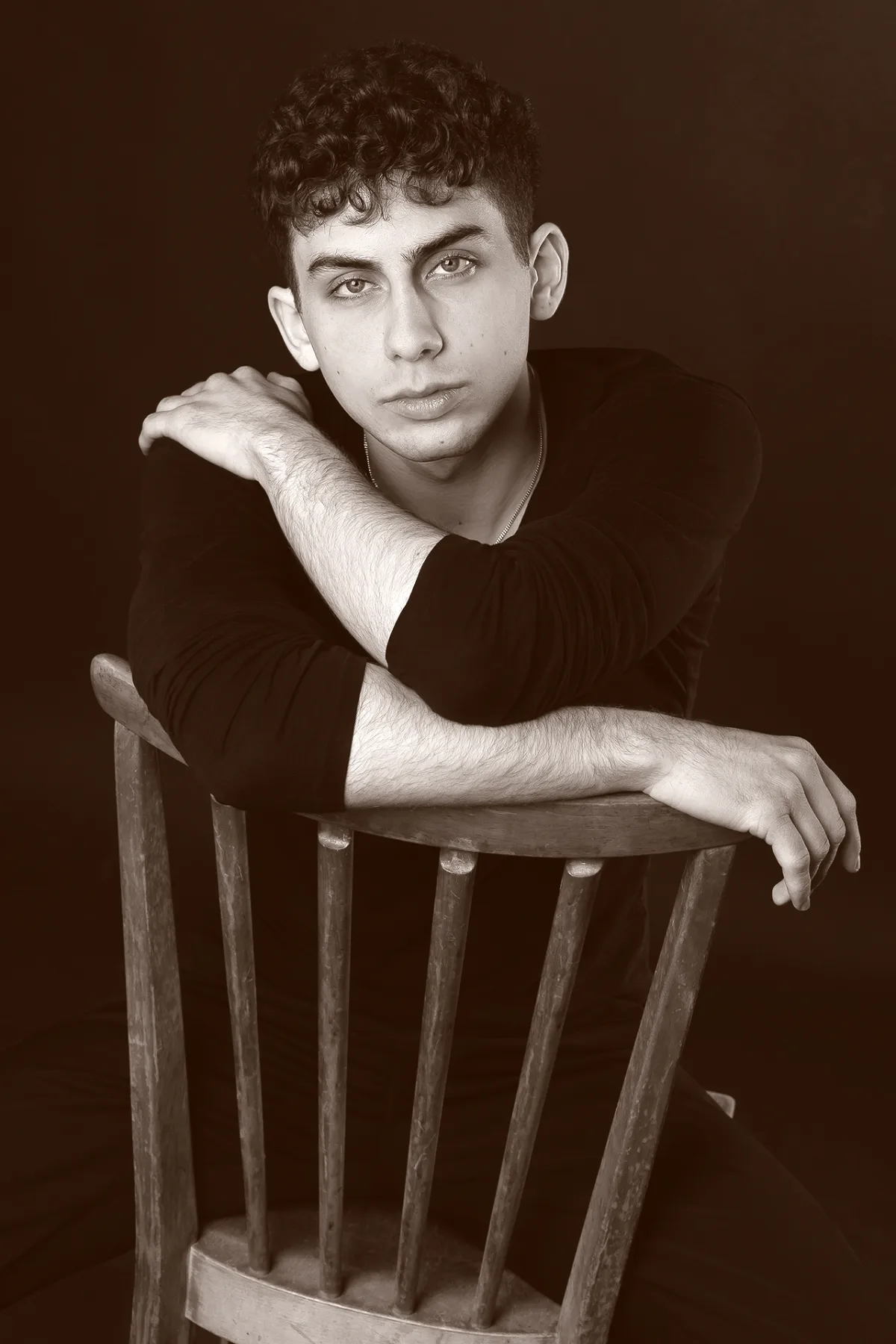 Sepia studio portrait of a young man resting his arms on the back of a chair