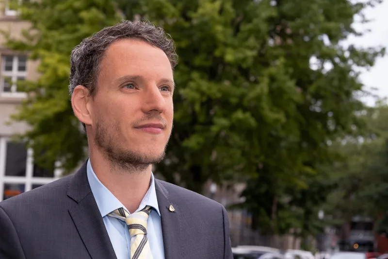 Outdoor business portrait: a man in a grey suit and striped tie in front of a soft green city backdrop