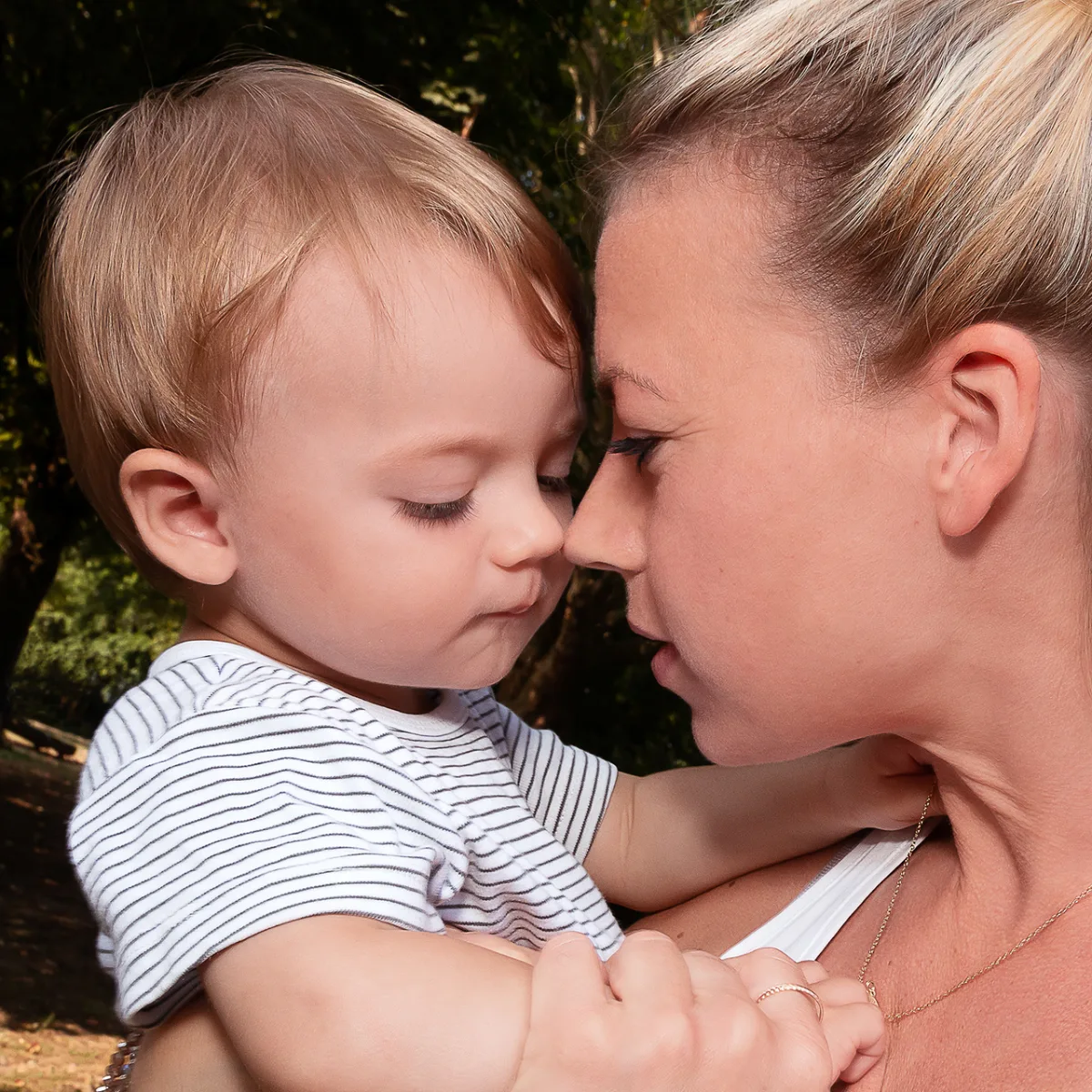 A blond toddler and his mother forehead to forehead in warm backlight