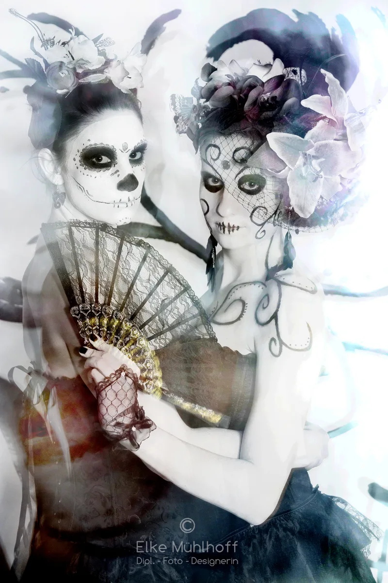 Zwei Frauen im 'Día de los Muertos'-Make-up mit üppigem Blumenkopfschmuck und Spitzenfächer