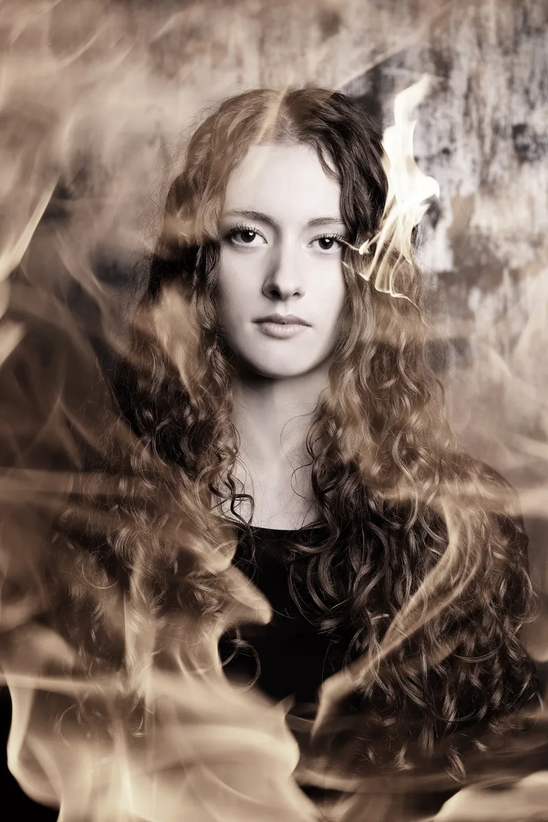 The same fire portrait in a warm sepia tone, flames and smoke around her face