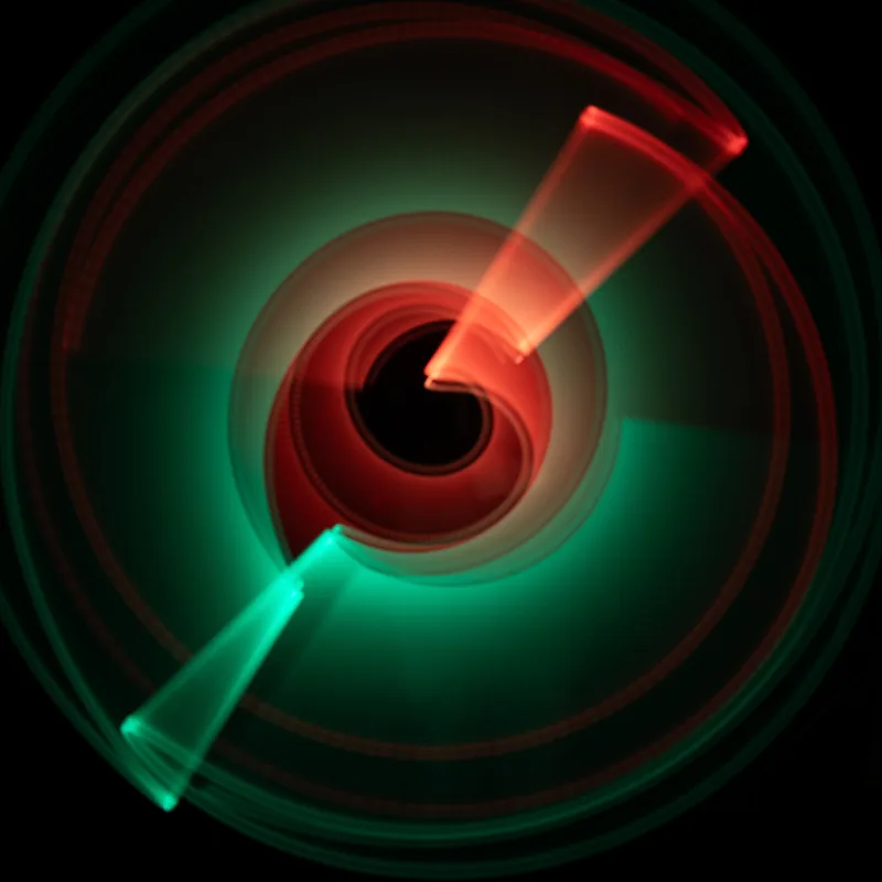 Light painting: red and green light trails forming a vortex on a black ground
