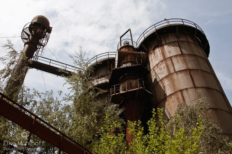 Stillgelegter Hochofen-Komplex mit Treppen und Stahlbehältern, von unten gegen den Himmel fotografiert