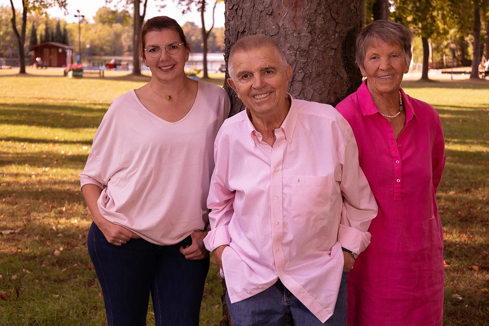 Family portrait in the park: two women and a man in shades of pink in front of a tree by a lake in Duisburg